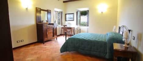 Quarto com cama, vigas de madeira, cômoda, escrivaninha e janela.