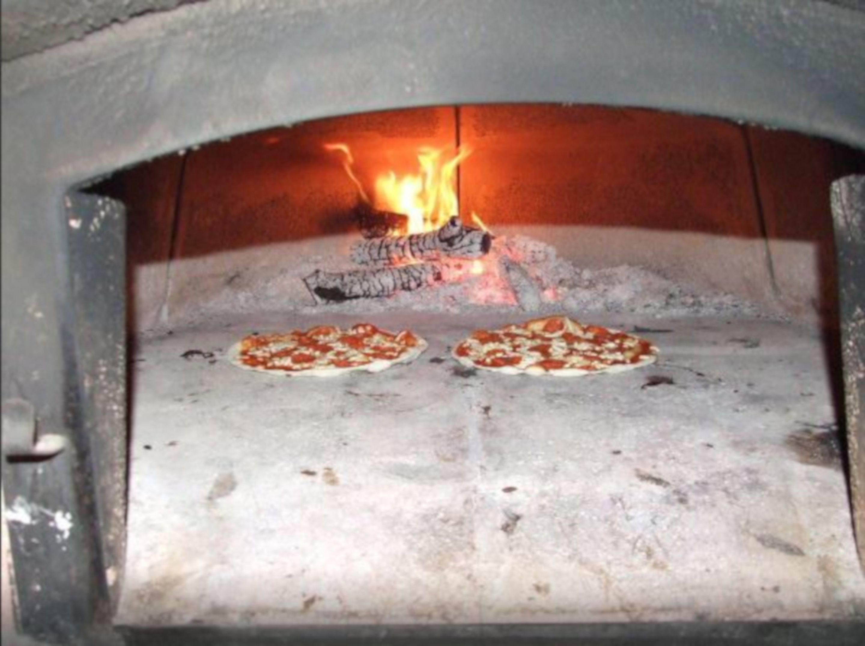 A wood-fired pizza oven with two pizzas being cooked.