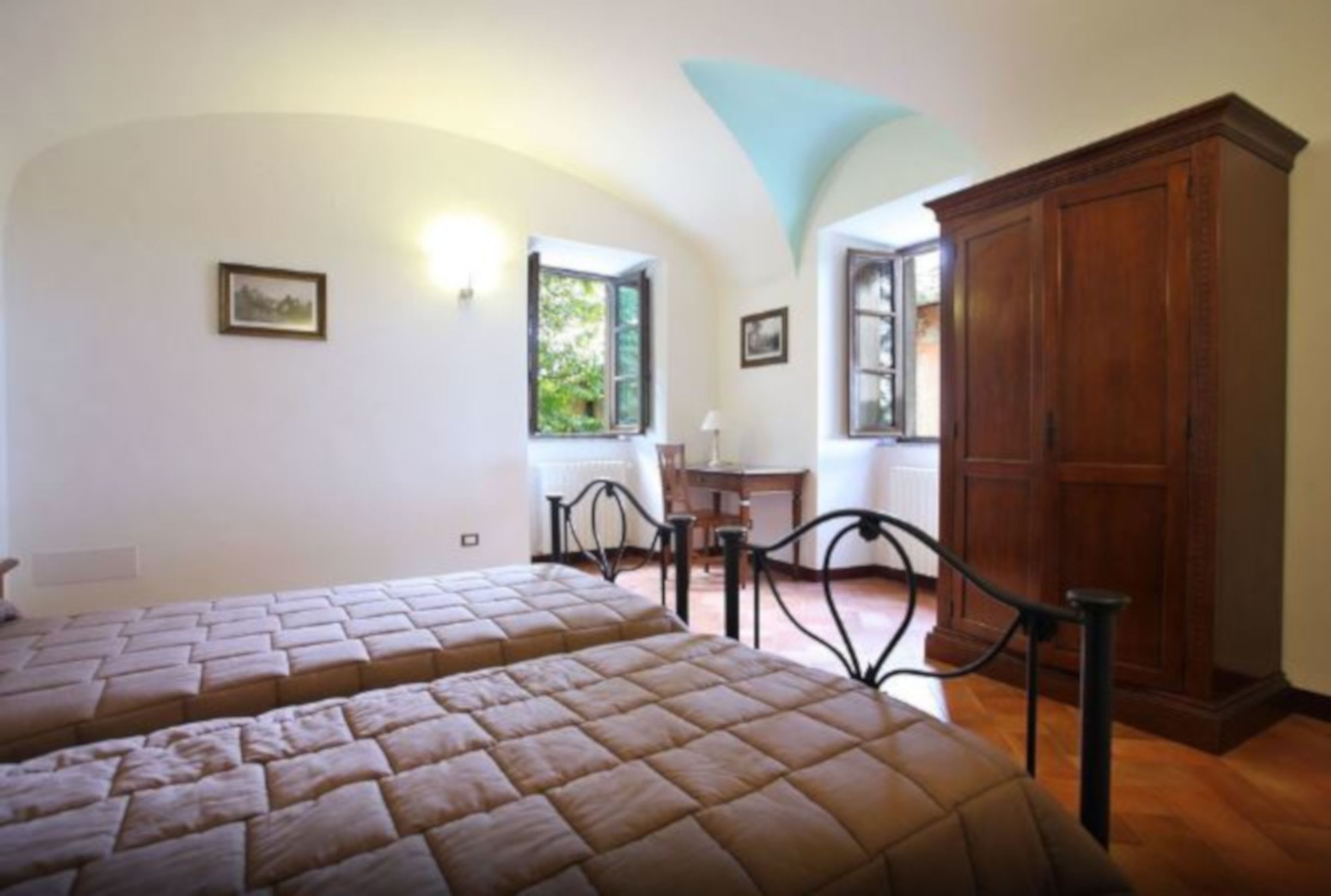 A bedroom with two beds, a wooden wardrobe, and a desk with a chair.