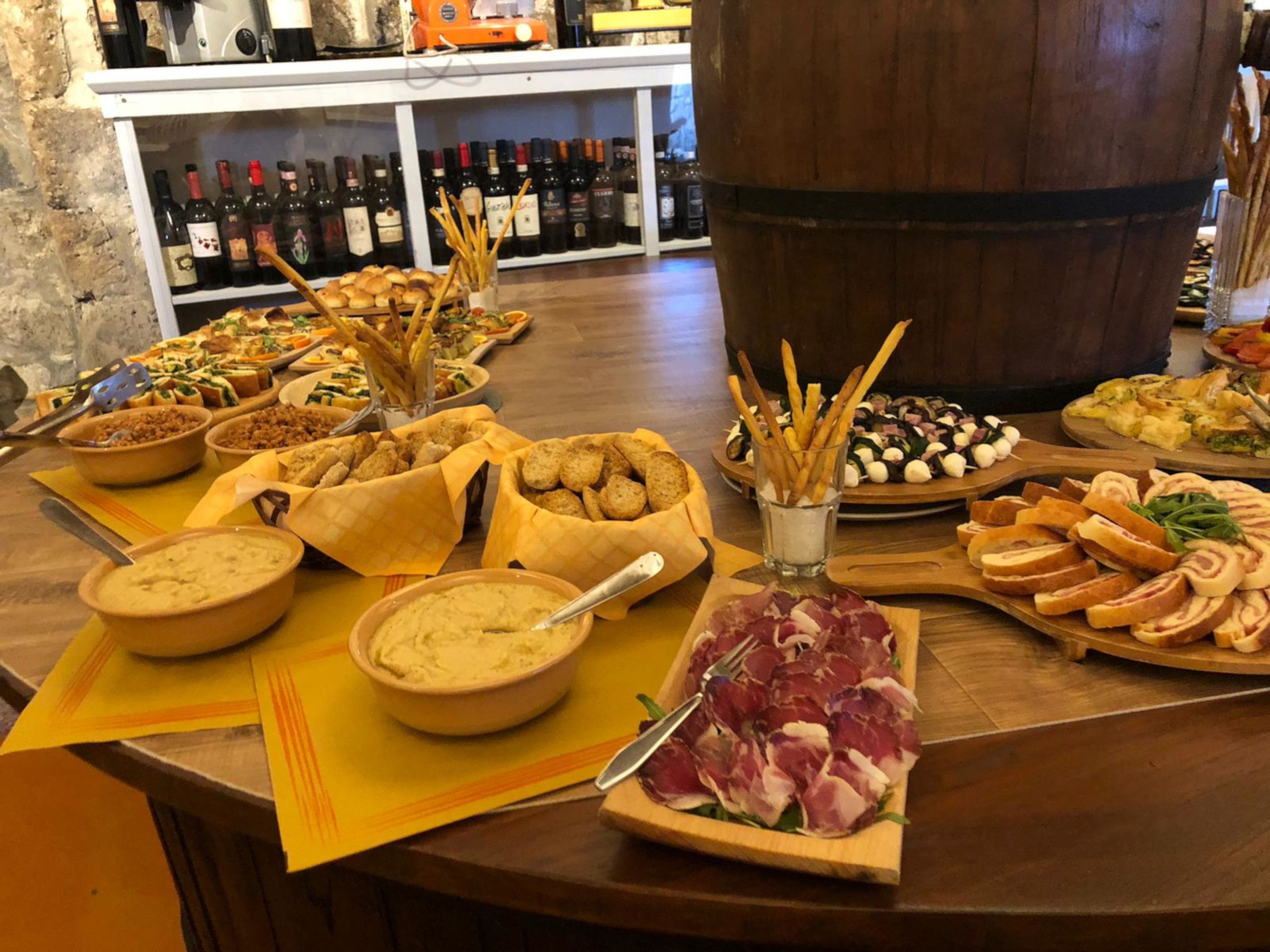 Una mesa de buffet con diversos alimentos y una estantería para vinos al fondo.