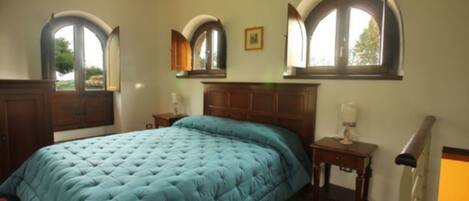 A bedroom with a large bed, two bedside tables, a nightstand, and a window with an arched design.