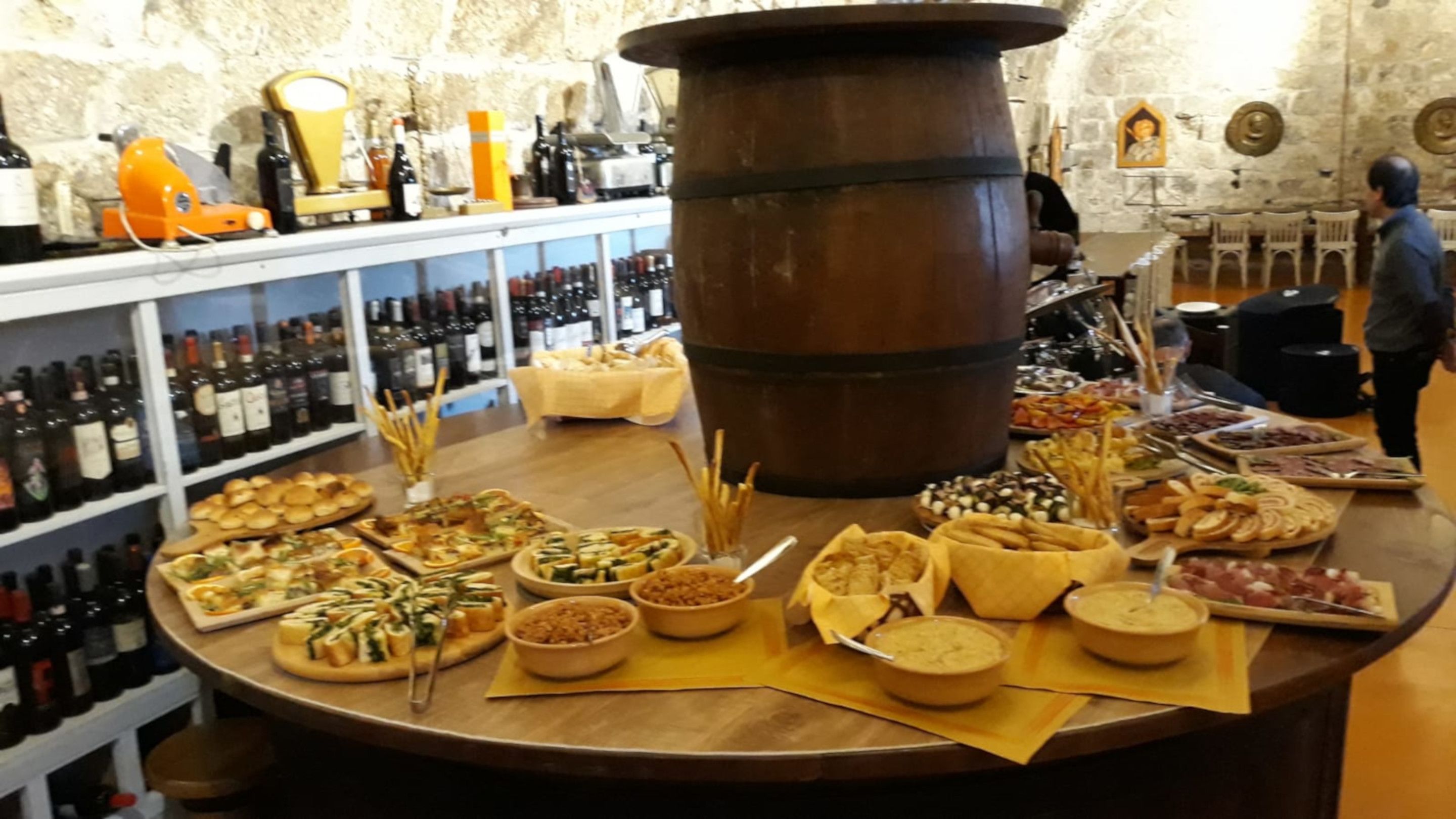 A bar area with a variety of food and drink options, including cheeses, breads, and a large barrel.