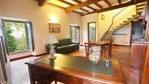 Una habitación amplia con un escritorio de madera, un sofá verde, una mesa de comedor y una escalera que sube a un nivel superior.
