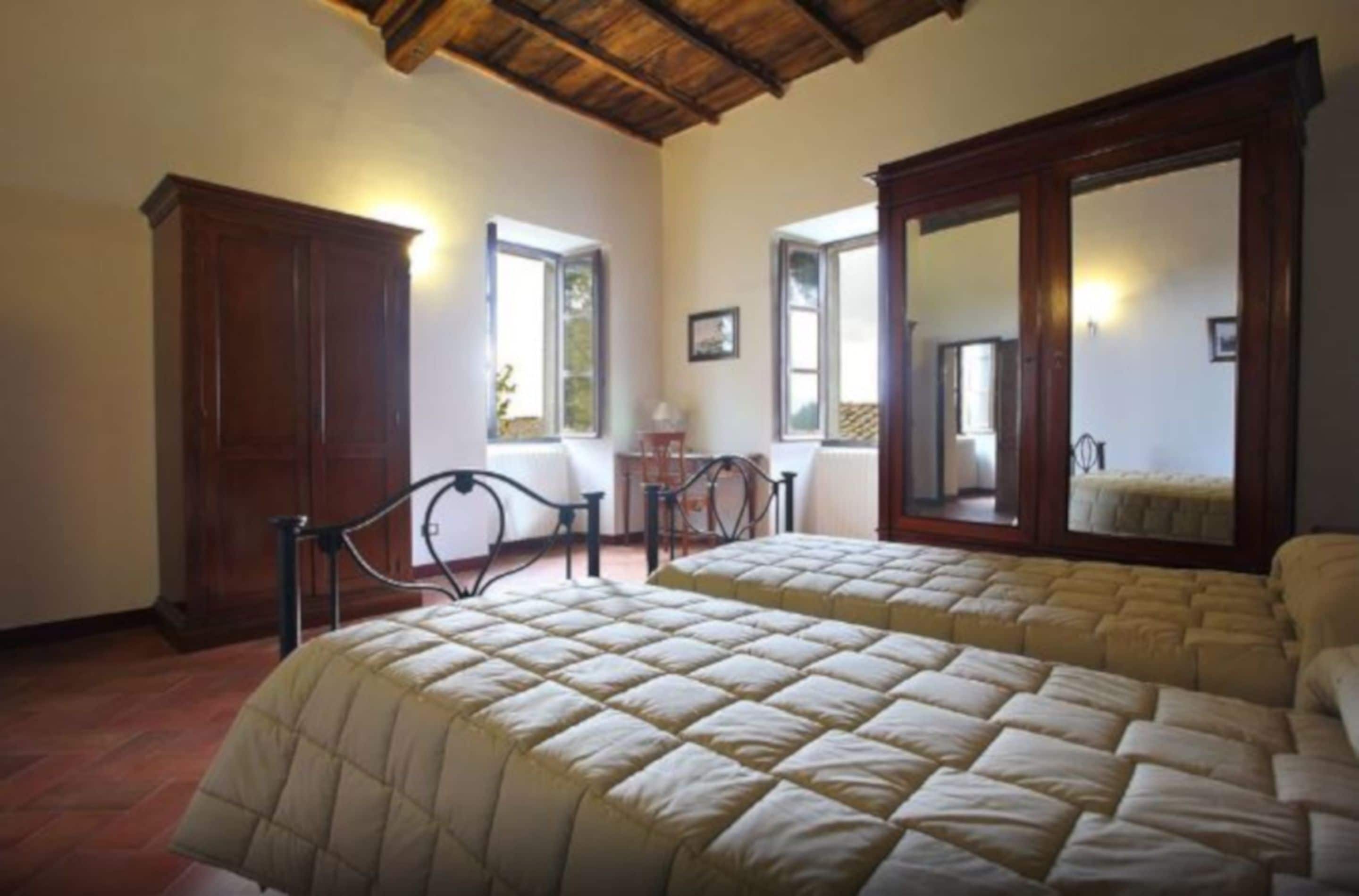 A bedroom with a large bed, wooden wardrobe, and a mirror.