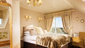 A bedroom with a large bed, a chandelier, curtains, and a view of the outdoors. - Castle Murray House Boutique B&B (Dunkineely)