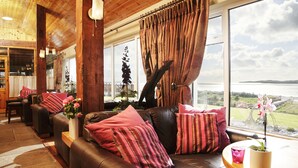 A cozy living room with a leather sofa, a wooden coffee table, and a large window with curtains. - Castle Murray House Boutique B&B (Dunkineely)