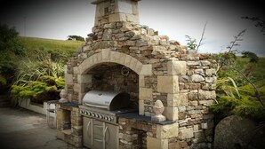 A stone-built outdoor kitchen with a built-in grill and storage cabinets. - Castle Murray House Boutique B&B (Dunkineely)