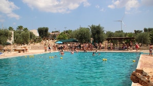Ein Swimmingpool mit klarem, blauem Wasser, umgeben von Bäumen und einer Windkraftanlage im Hintergrund.