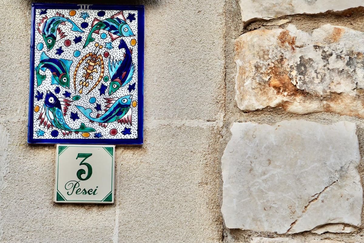 Un azulejo decorativo montado en la pared con un motivo de pez y una placa con un número de casa debajo.