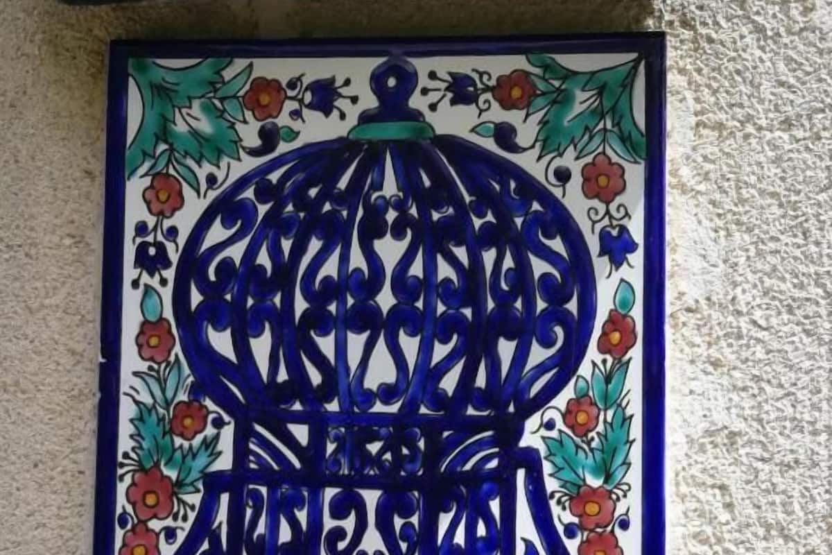 Una placa decorativa en la pared con un diseño azul y blanco, que presenta caligrafía árabe y motivos florales. Debajo, una placa blanca con texto verde que dice '2 Gabbia'.