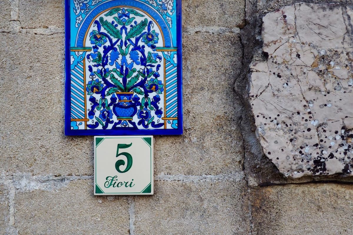 Un azulejo decorativo con motivos florales y una pequeña placa debajo con el número 5 y la palabra 'Fiori'.