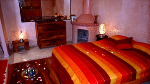 Quarto com uma cama grande, cômoda de madeira, espelho, lareira e duas mesas de cabeceira com luminárias.