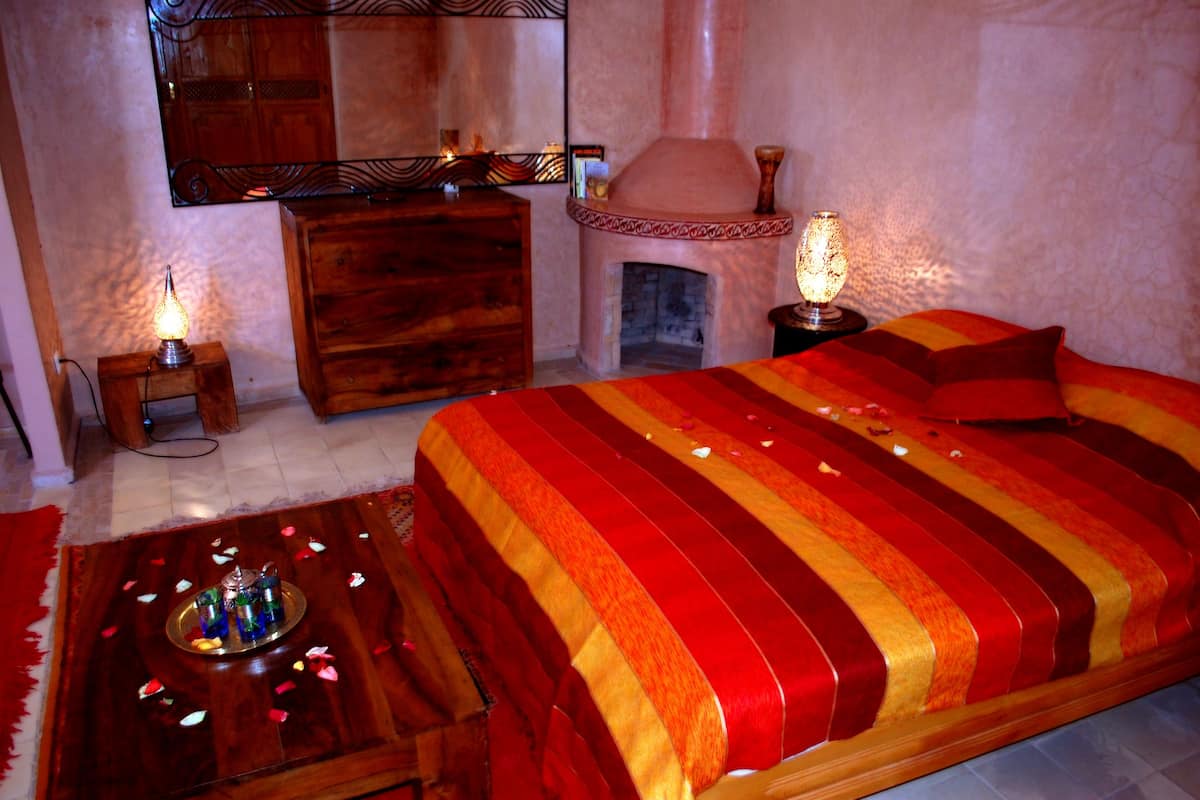 A room with a large bed, a wooden dresser, a mirror, a fireplace, and two bedside tables with lamps.