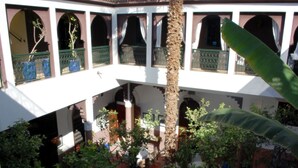 Um pátio com uma coluna central, arcos e plantas em vasos.