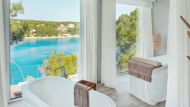 A modern bathroom with a freestanding bathtub, large windows offering a view of a pool and a coastal landscape. - Gava Waterman Milna Resort (Milna)