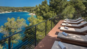 A deck with sun loungers overlooking a coastal area with clear blue waters and dense green trees. - Gava Waterman Milna Resort (Milna)
