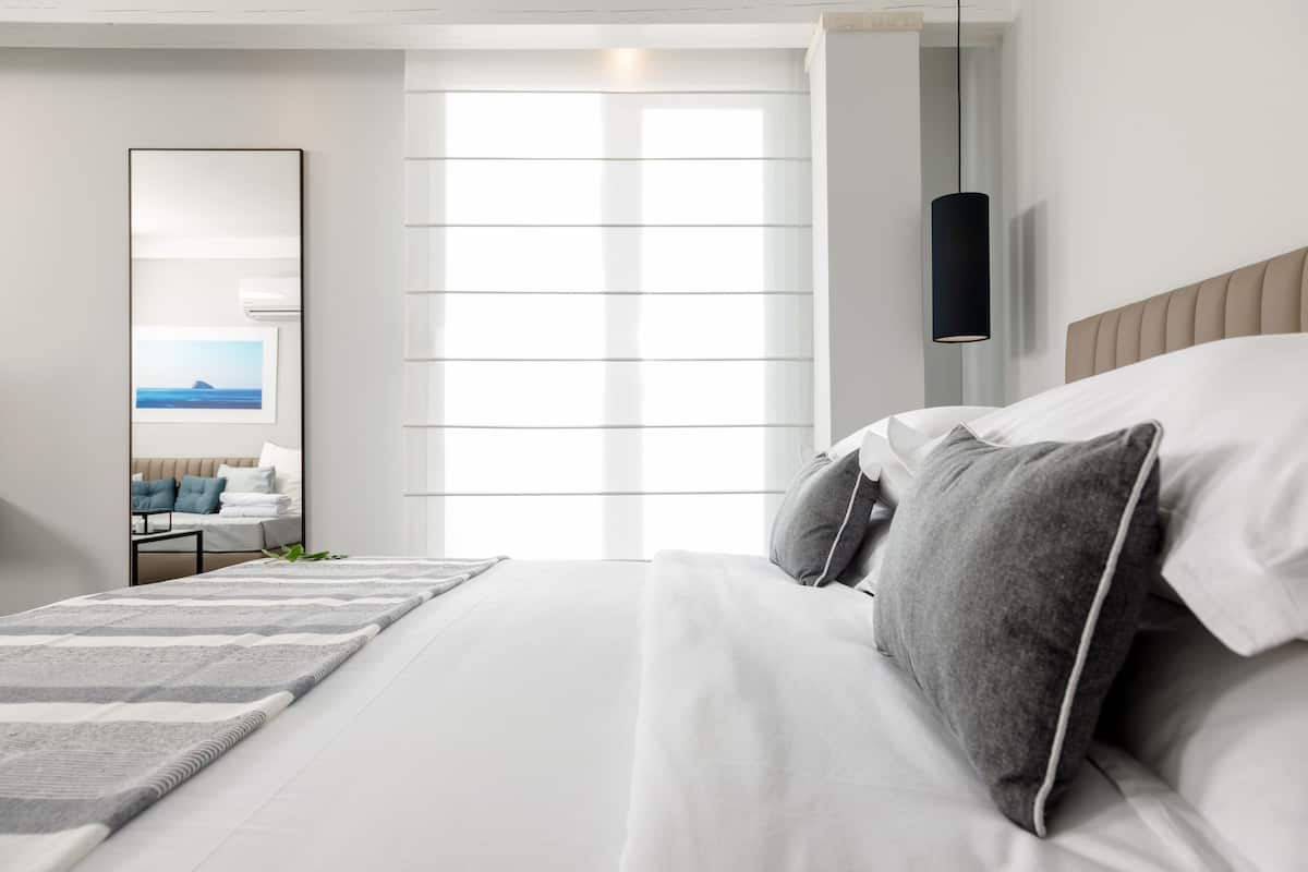 Moderni hotellihuone, jossa on suuri sänky, yöpöytä, peili ja näkymä ulos.
