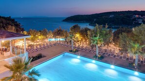 A swimming pool with lounge chairs and palm trees, overlooking a body of water and a hillside. - Gava Waterman Milna Resort (Milna)
