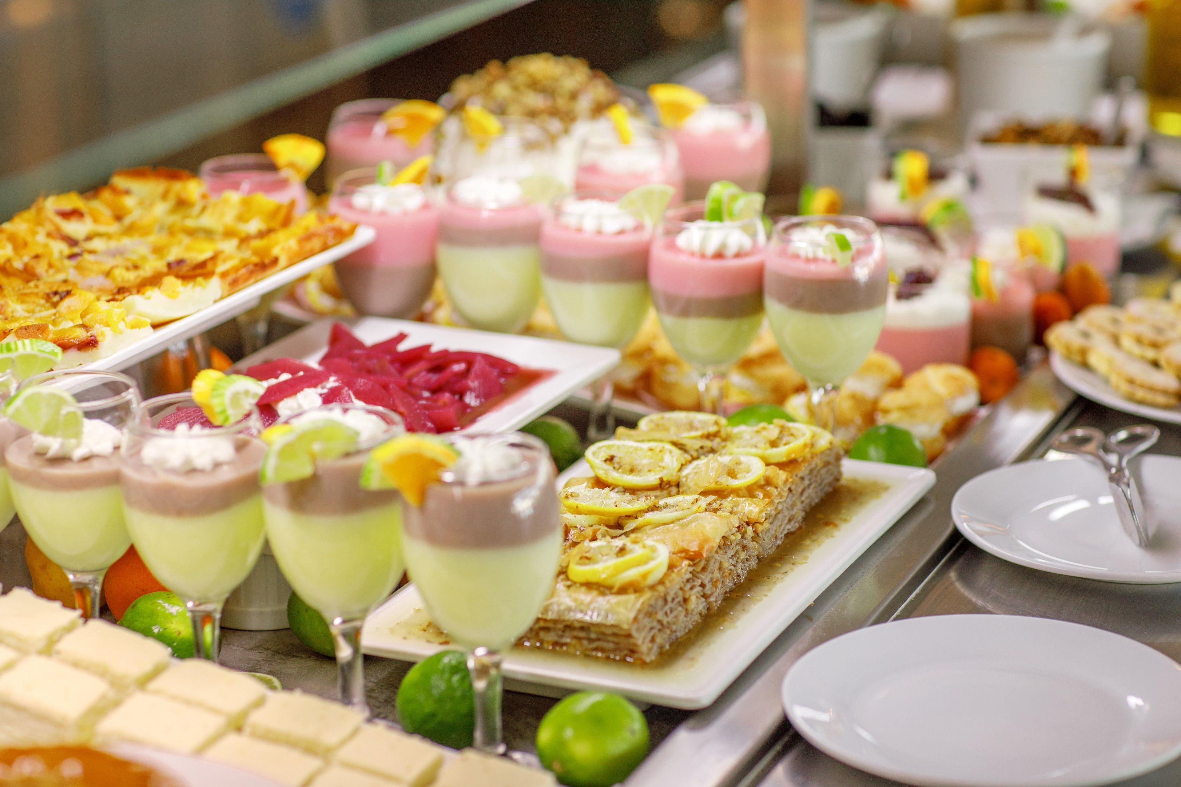 A buffet with various desserts and drinks, including layered desserts in glasses and a rectangular dessert on a plate.