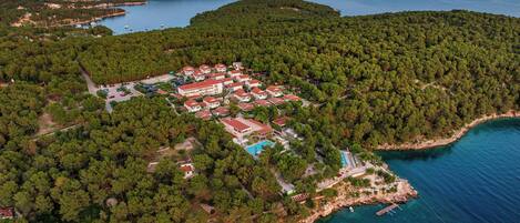 An aerial view of a coastal resort with multiple buildings, a swimming pool, and boats in the water.