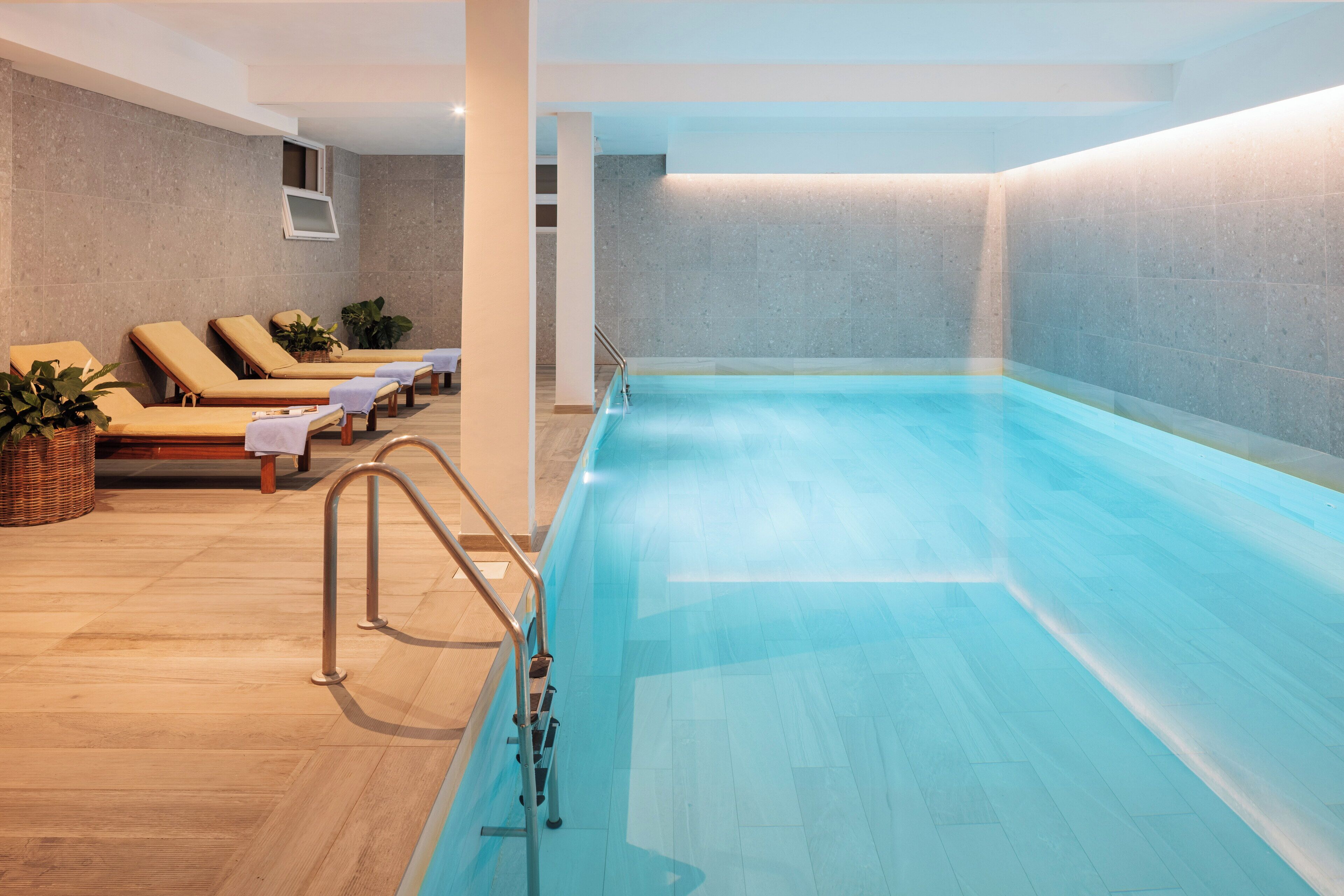 A modern indoor swimming pool with lounge chairs and a wooden floor.