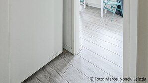 Un couloir mène à une pièce où se trouvent un bureau blanc, une chaise et un téléviseur.