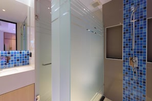 A modern bathroom with a glass shower enclosure, a blue-tiled shower area, and a white sink with a mirror.
