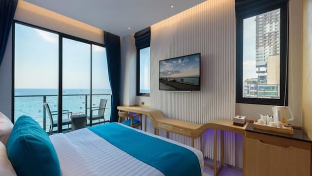 A hotel room with a large bed, a desk, a chair, a TV, and a view of the sea. - Deep Blue Z10 Pattaya (Pattaya)