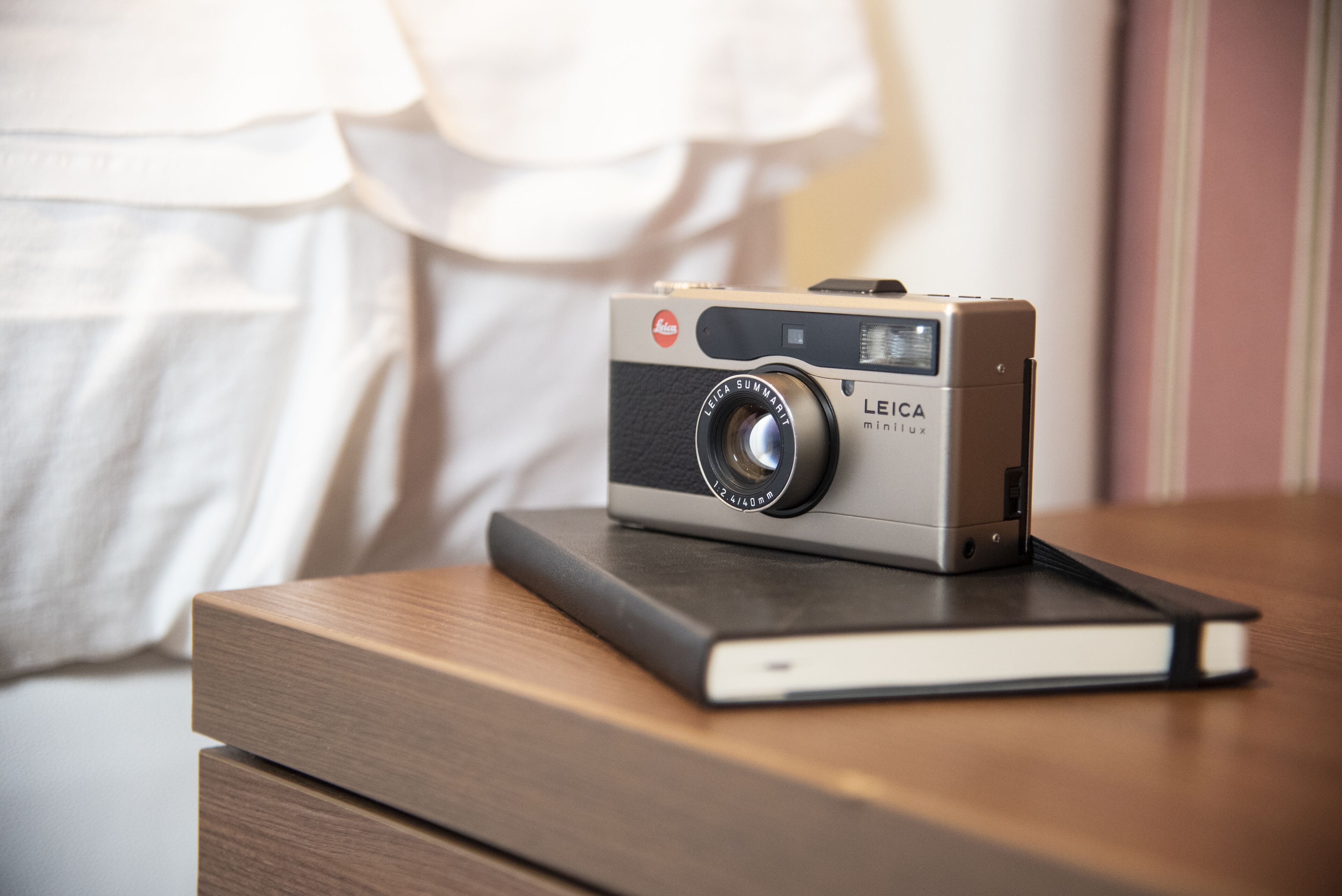 A Leica Minilux camera on a wooden surface with a book.