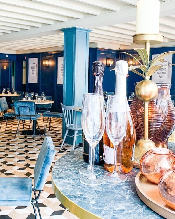 Interior de un restaurante con suelo a cuadros, sillas azules y mesas dispuestas con copas y botellas de vino.