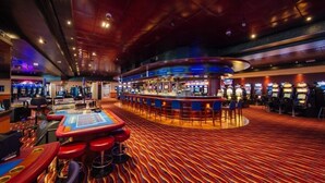 A casino with a red carpet, multiple gaming tables, and a bar area. - Hotel Franky (Blankenberge)