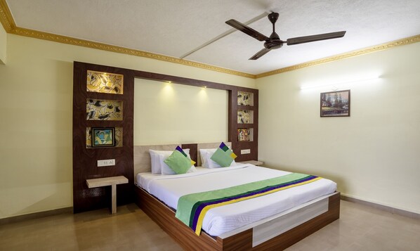 A bedroom with a bed, a ceiling fan, a nightstand, and wall art. - Itsy Hotels Vijaya Residency (Udupi)