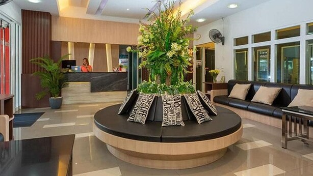 A reception area with a central floral arrangement, a reception desk, and a seating area with a sofa. - The Ring Residence (Hat Yai)