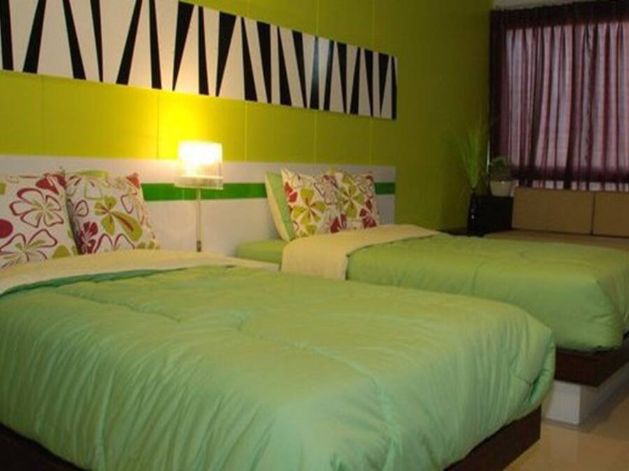 Habitación de hotel con dos camas, cabecero verde y blanco, pared con diseño geométrico y ventana con cortinas.