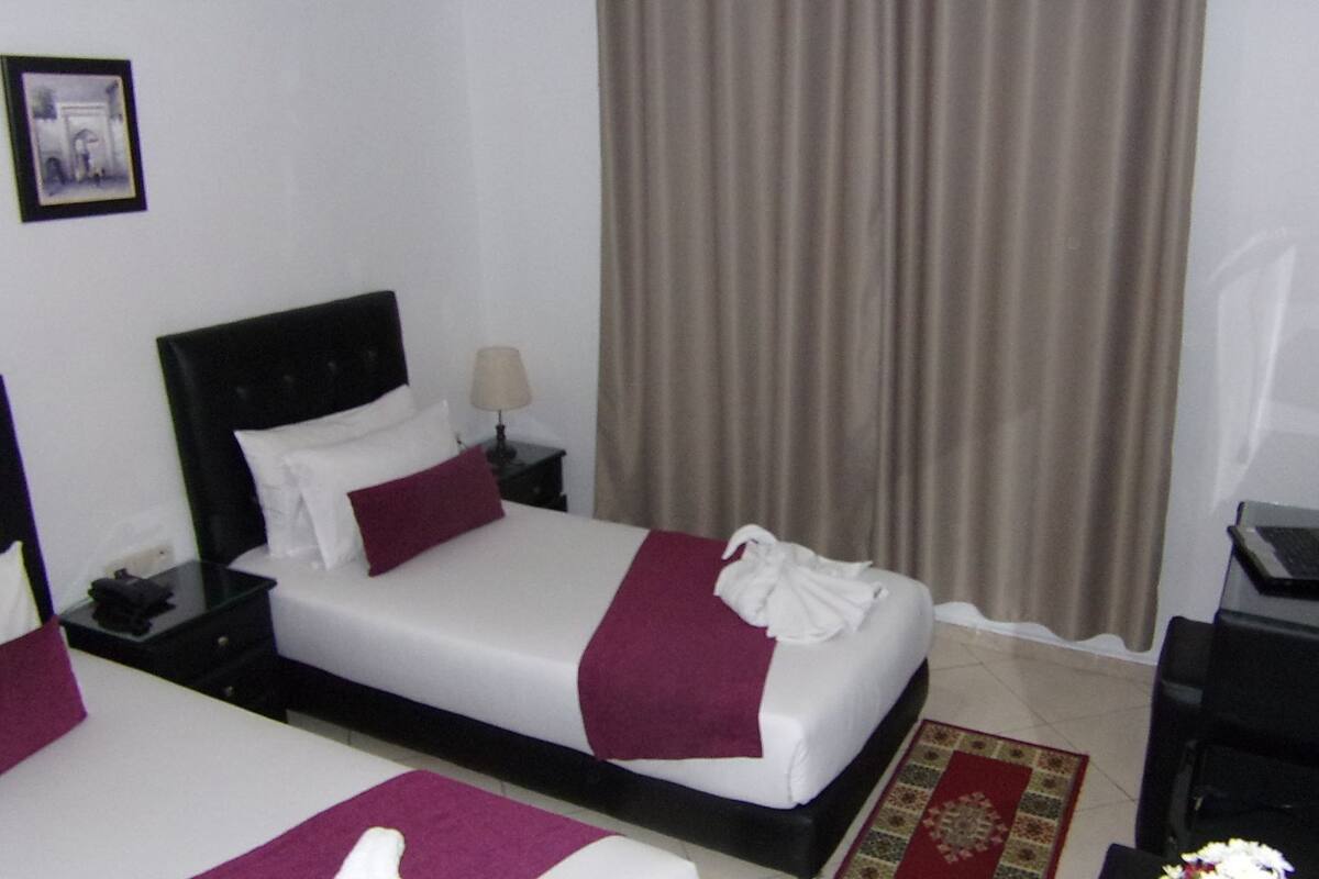 A hotel room with two beds, a nightstand with a lamp, a desk with a laptop, and a framed picture on the wall.