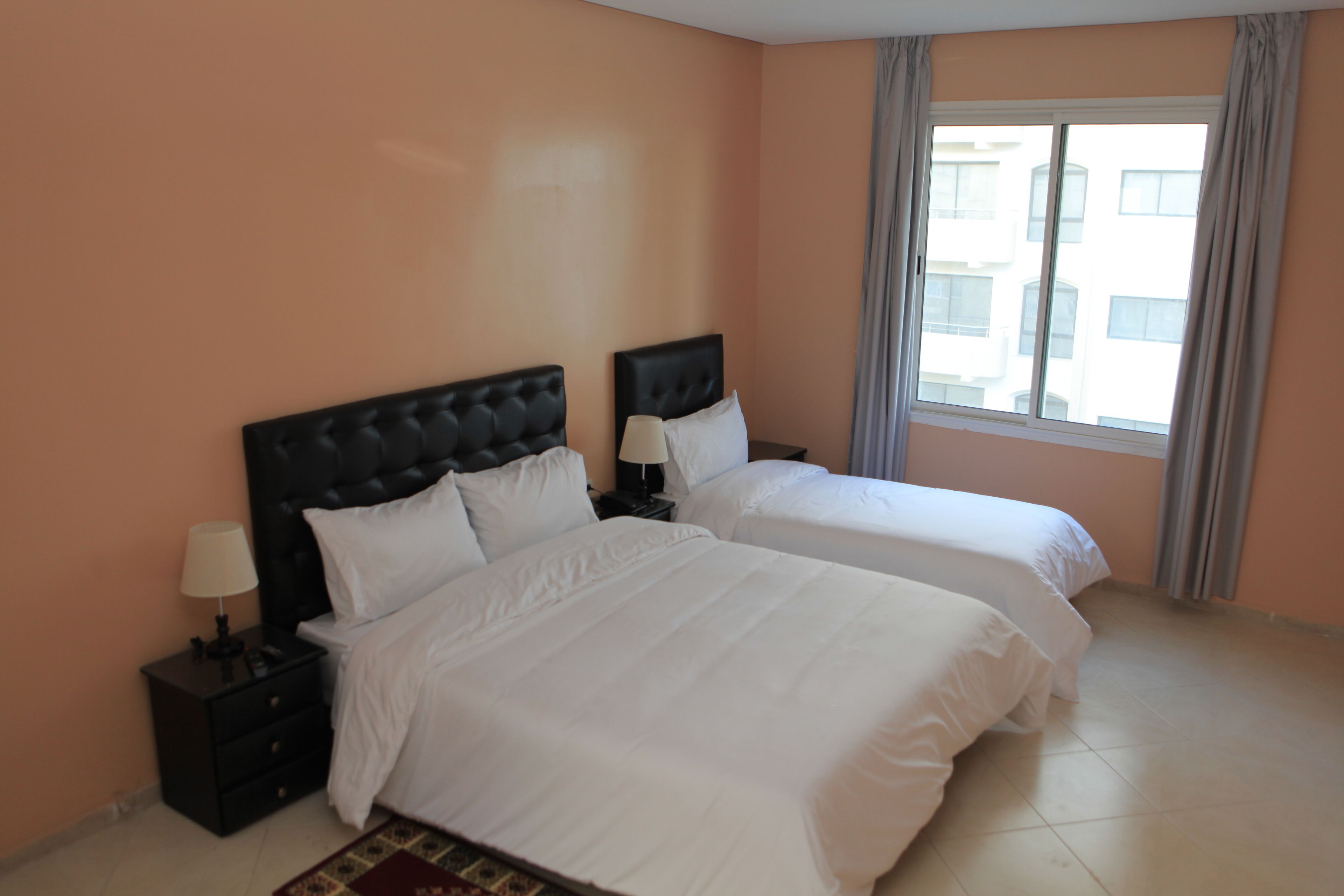 Una habitación de hotel con dos camas, una mesita de noche con lámpara y una ventana con cortinas.