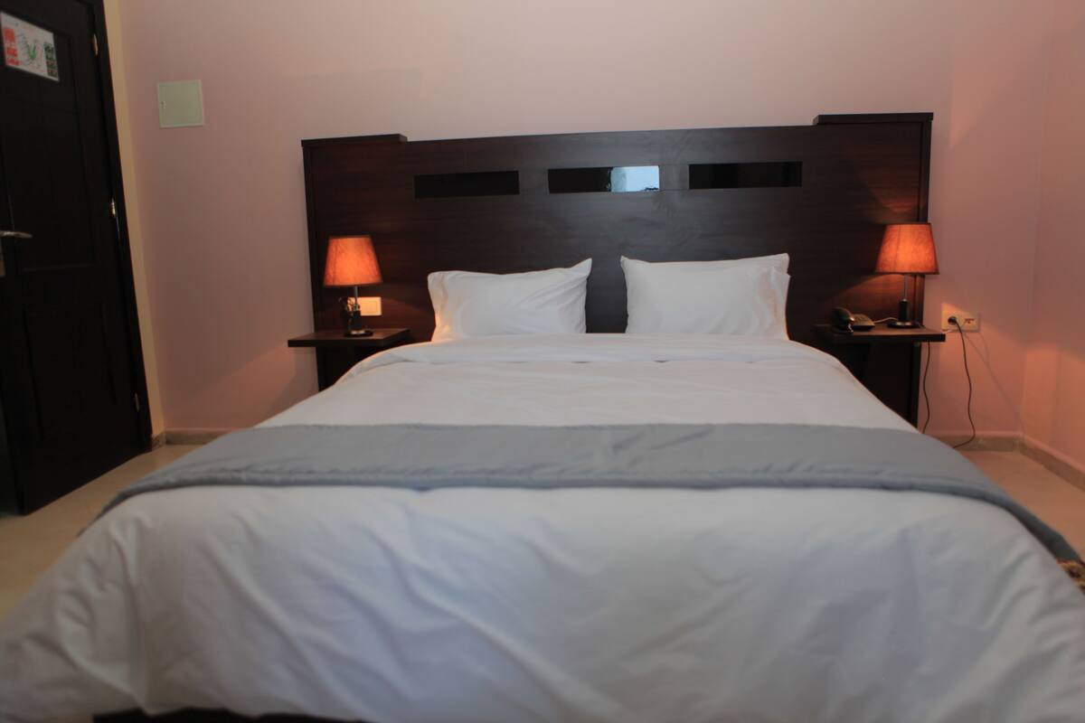 A hotel room with a large bed, two bedside tables with lamps, and a dark headboard.