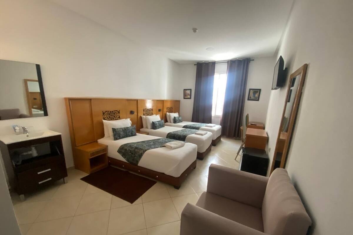 A hotel room with three beds, a sofa, a TV, and a bathroom with a mirror and sink.