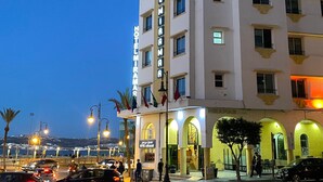 Un hotel con un letrero vertical llamativo, varios balcones y una entrada bien iluminada.
