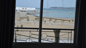 Vista desde una ventana que da a una playa con un muelle, un edificio blanco y un cielo despejado.