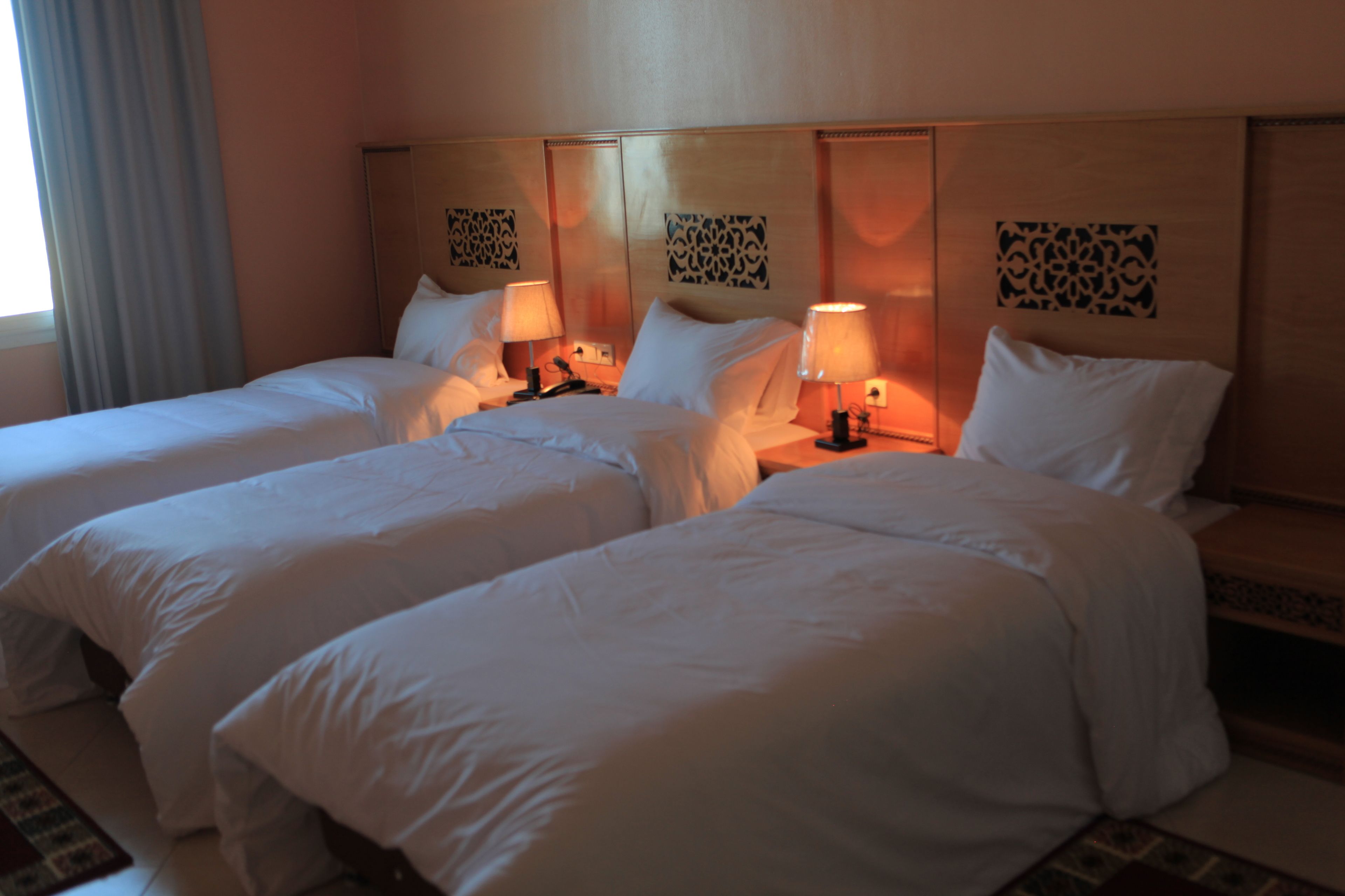 Une chambre d’hôtel avec trois lits, chacun étant équipé de draps blancs et de lampes sur les tables de chevet.