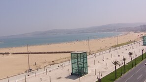 A beach with a clear view of the sea, a promenade with a glass structure, and a road alongside. - Hôtel Miramar (Tangier)