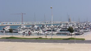 Un puerto deportivo con numerosas embarcaciones amarradas, cielo despejado y una grúa de construcción al fondo.