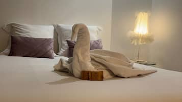 A neatly made bed with a towel folded in a swan shape, two toiletries, and a bedside lamp.