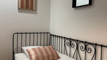A neatly made bed with a striped pillow and a blanket, a metal headboard, a wall-mounted mirror, and a framed artwork above the bed.