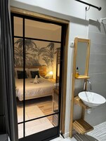 Quarto com cama, mesa de cabeceira, luminária e parede com mural tropical.