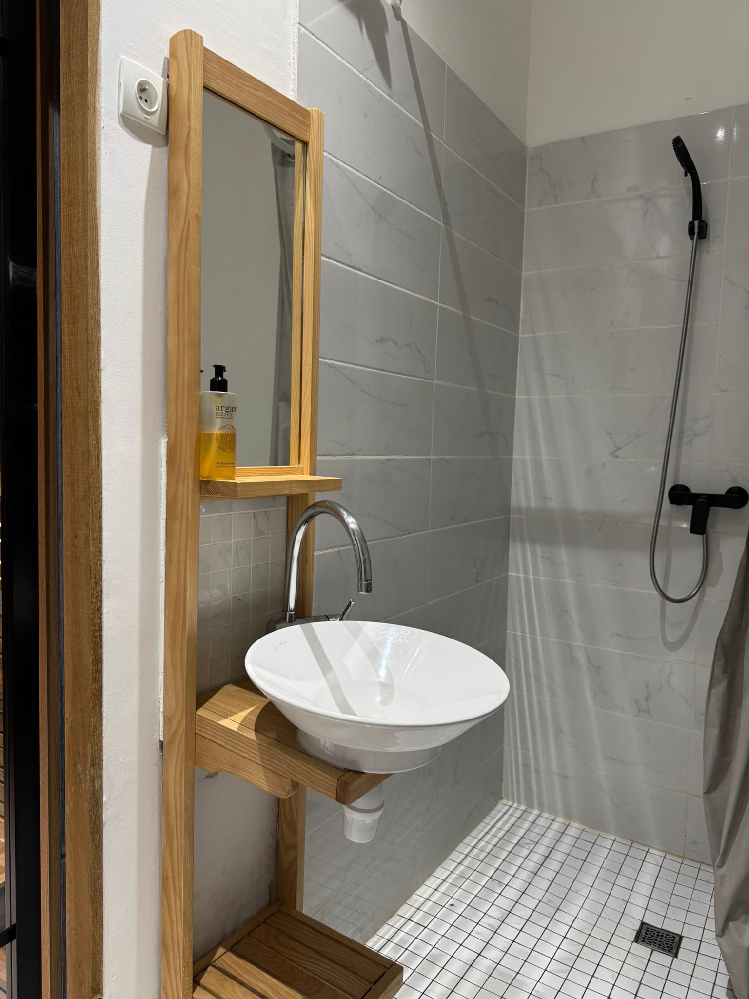 Un baño con tocador de madera, lavamanos blanco, espejo y zona de ducha.