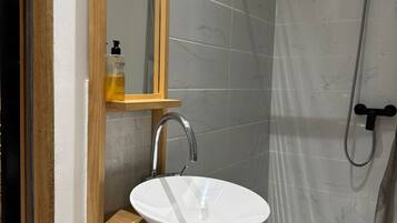Un baño con tocador de madera, lavamanos blanco, espejo y zona de ducha.
