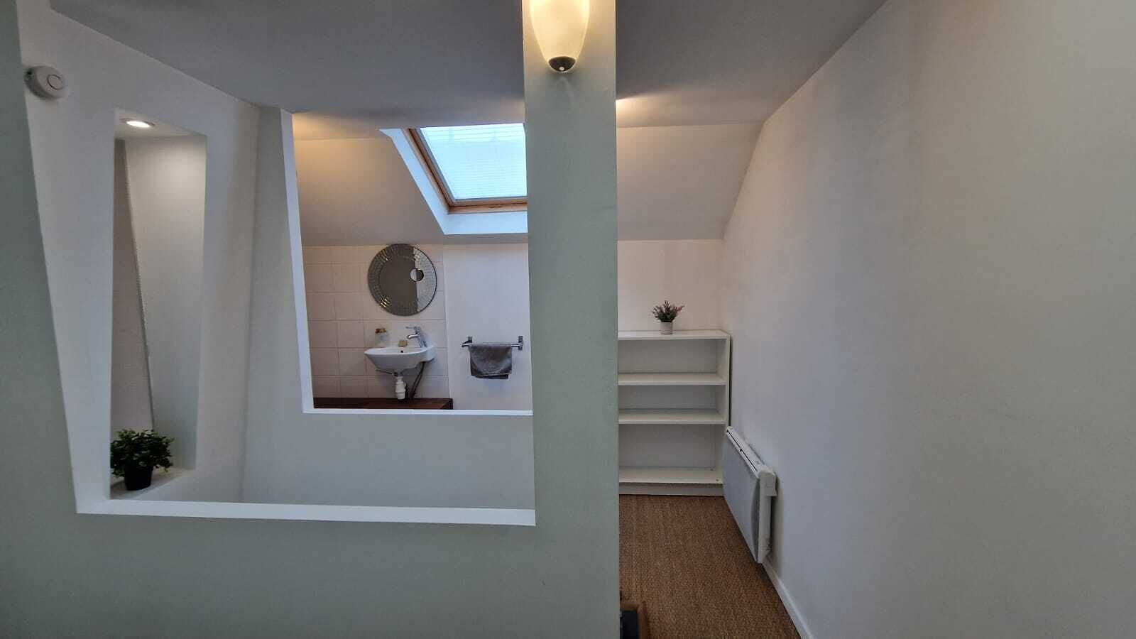A narrow hallway with a skylight, a small bathroom with a sink and mirror, and a radiator.