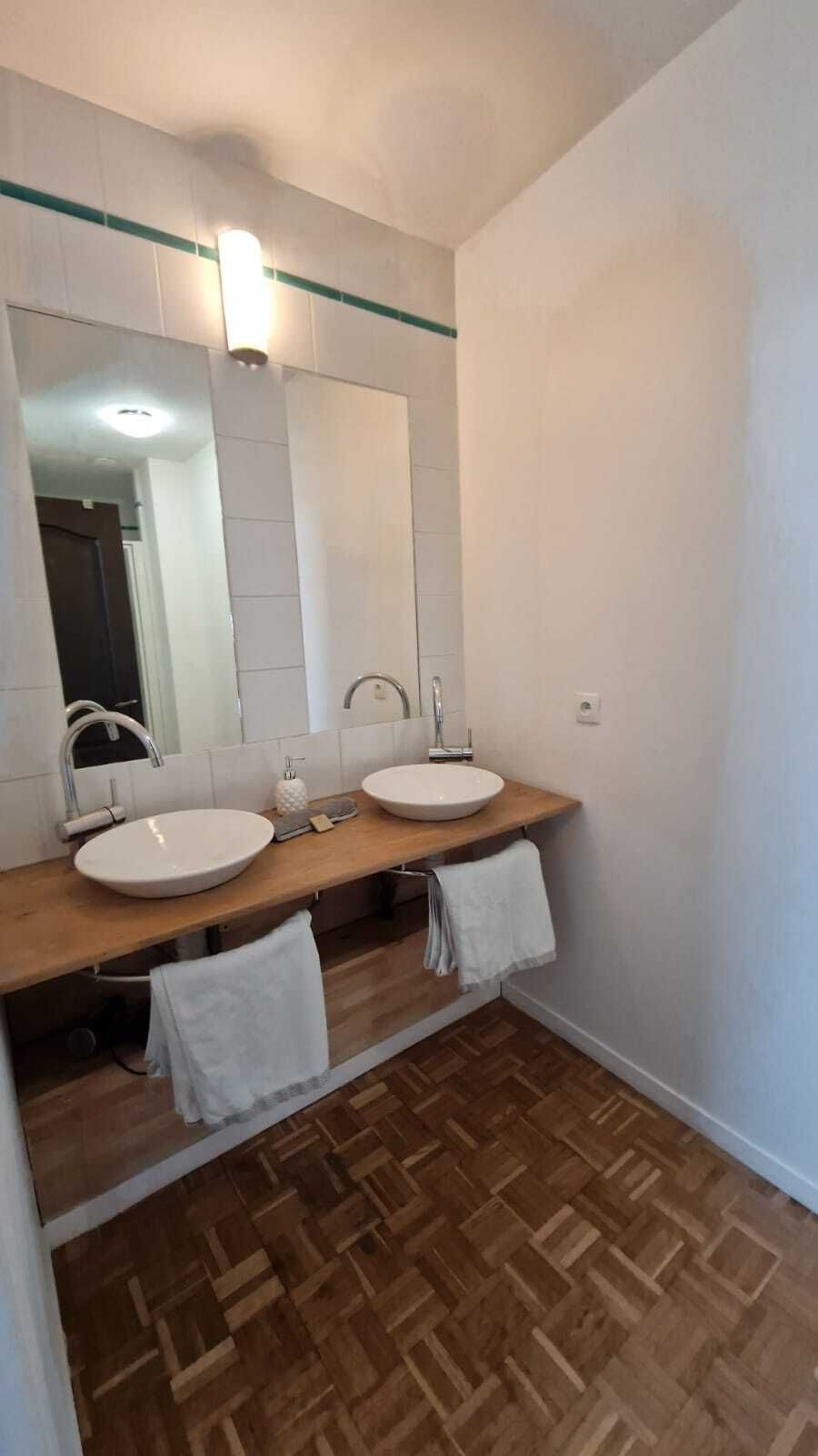 Un baño con dos lavamanos, un espejo y piso de madera.